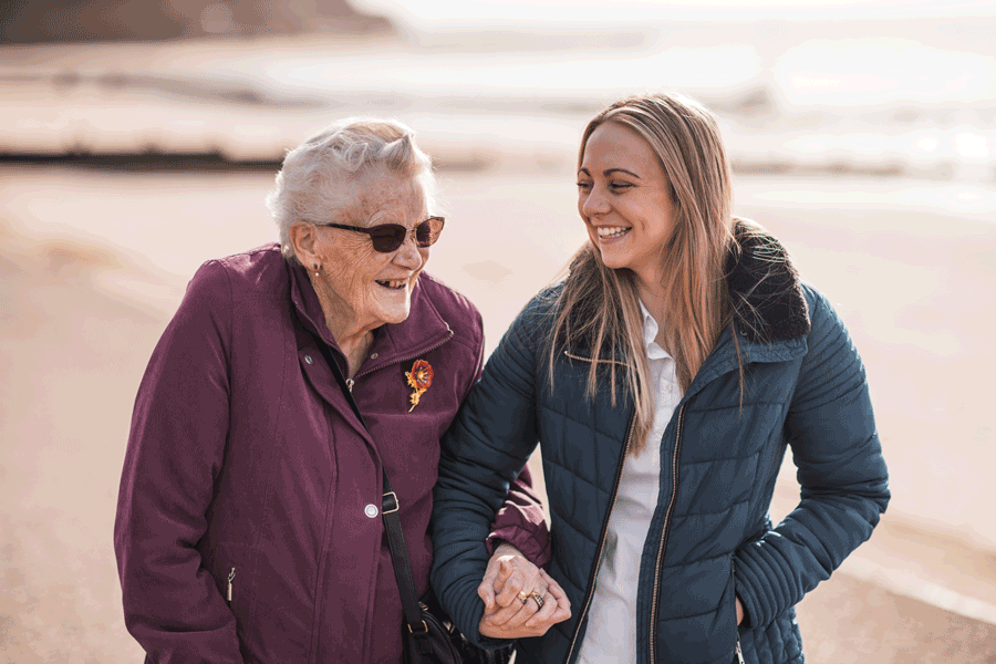 Care worker and client walking along the beach