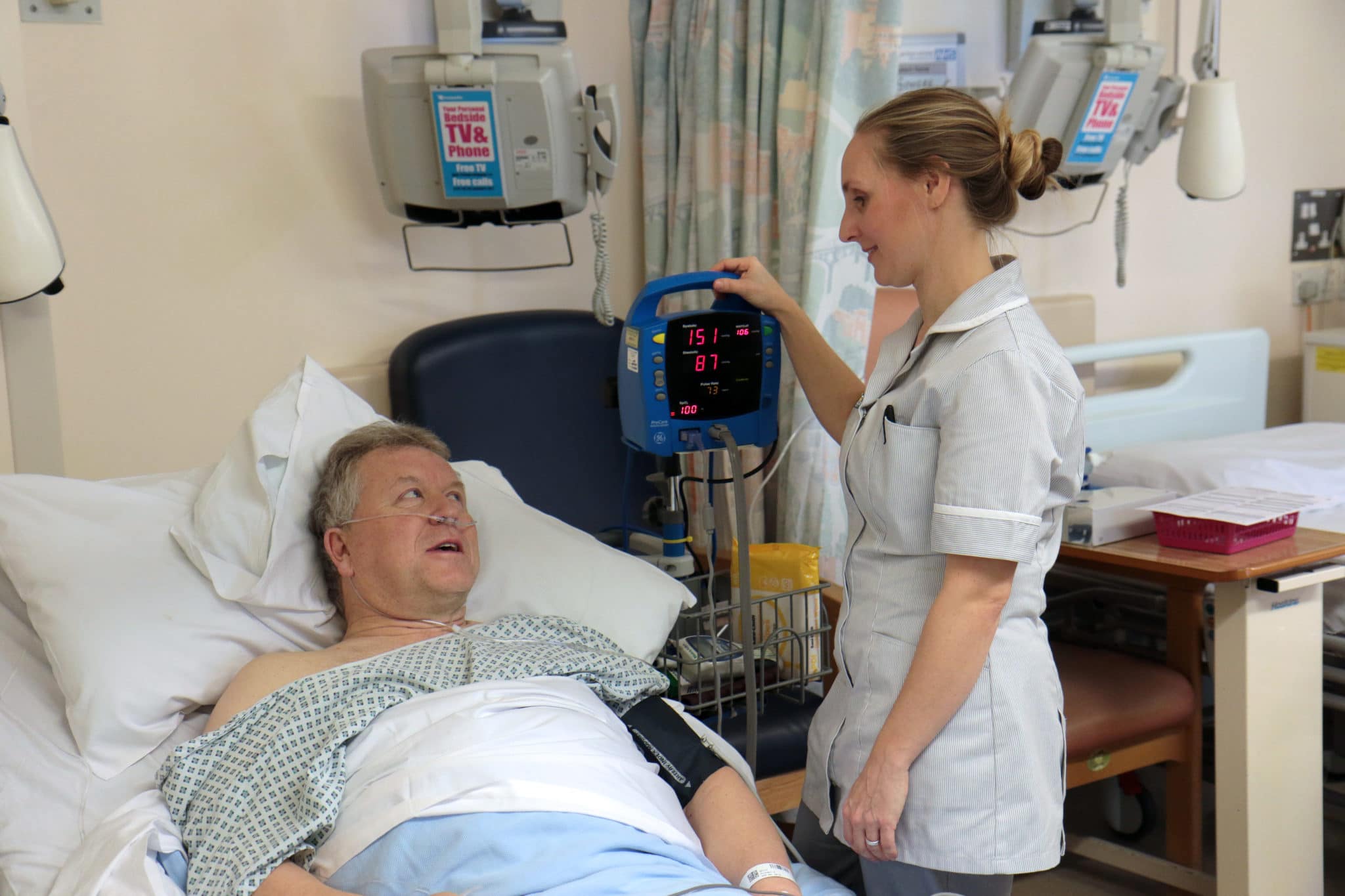 man in hospital bed with nurse checking