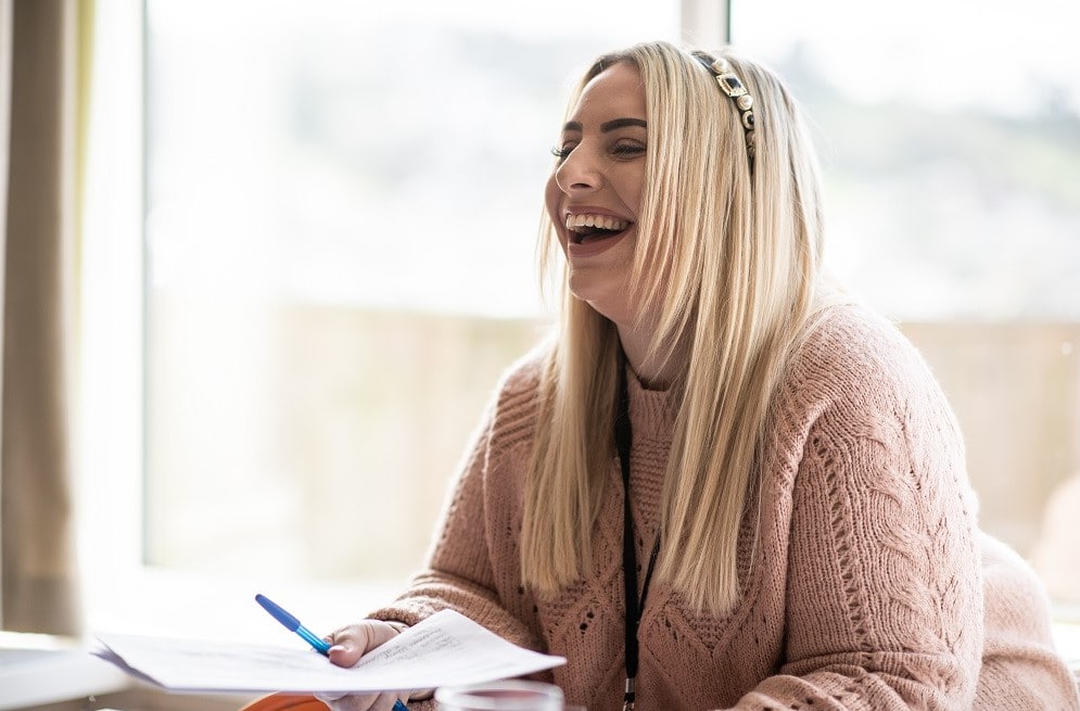 Multi-site registered manager, Lou, sat at a table holding some paper and laughing