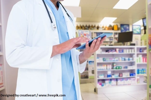 A pharmacist standing in a pharmacy looking at an electronic device