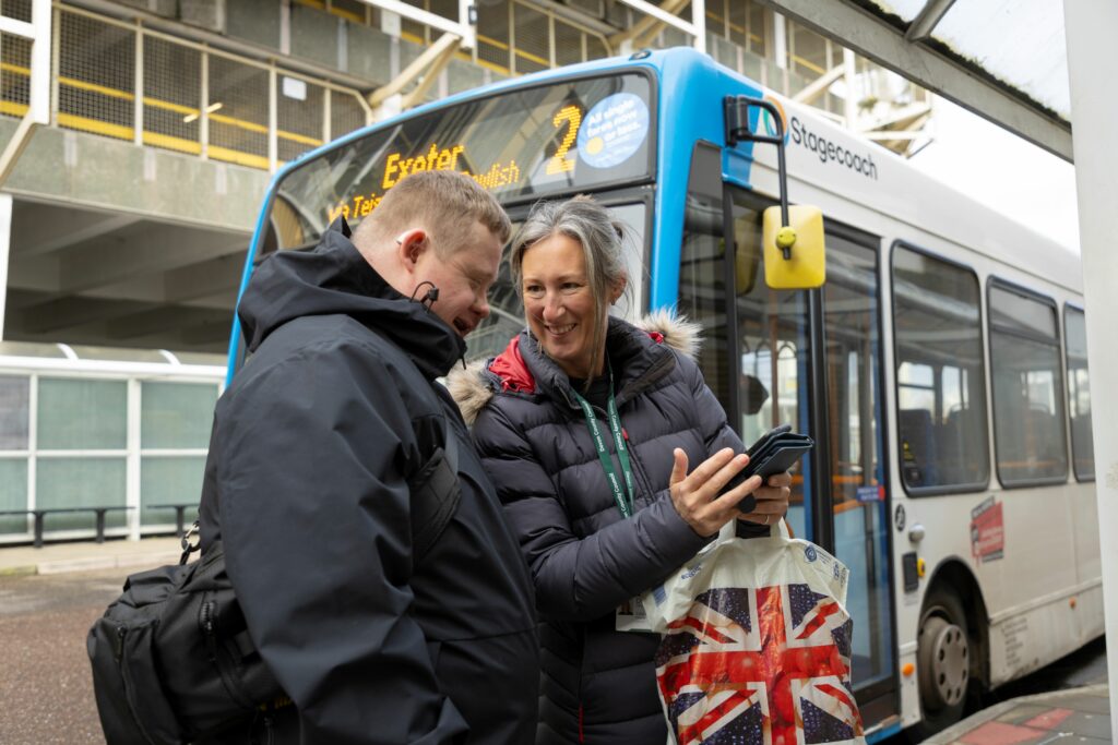 Two people looking at a phone by a bus