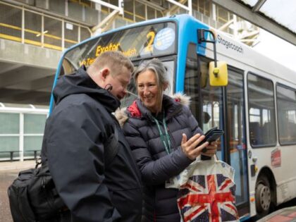 Two people looking at a phone by a bus