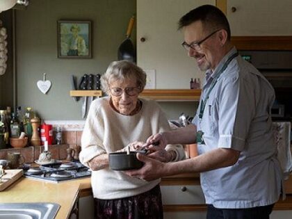 An older person holding a pan with support from an reablement worker