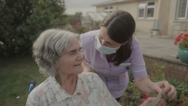 A older women in a wheelchair smiling at a carer wearing a face mask